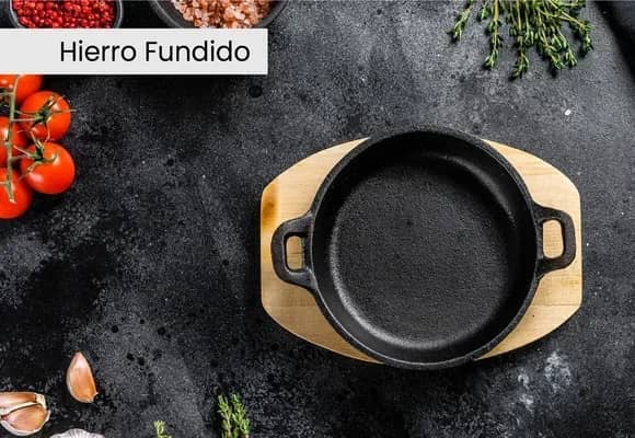 Hierro fundido: sartén de hierro con base de madera sobre una mesada oscura.